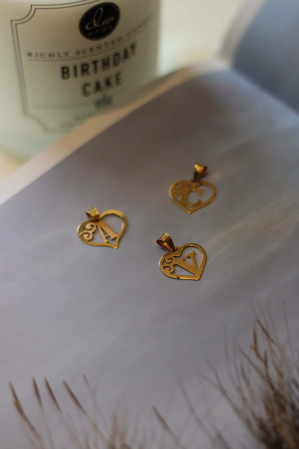 V Heart Initial Gold pendant displayed elegantly with decorative cake candle in background.