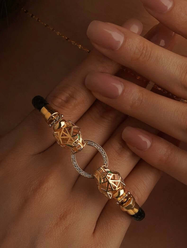 Gold bracelet with black accents on a hand against a neutral background