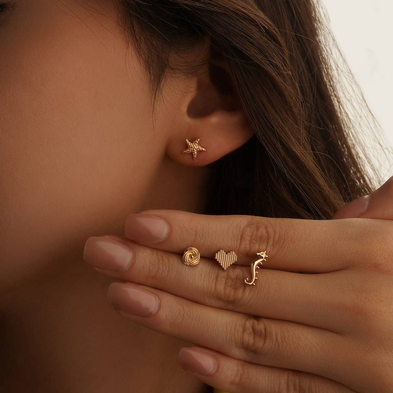 Close-up of a person wearing gold earrings and rings on a neutral background