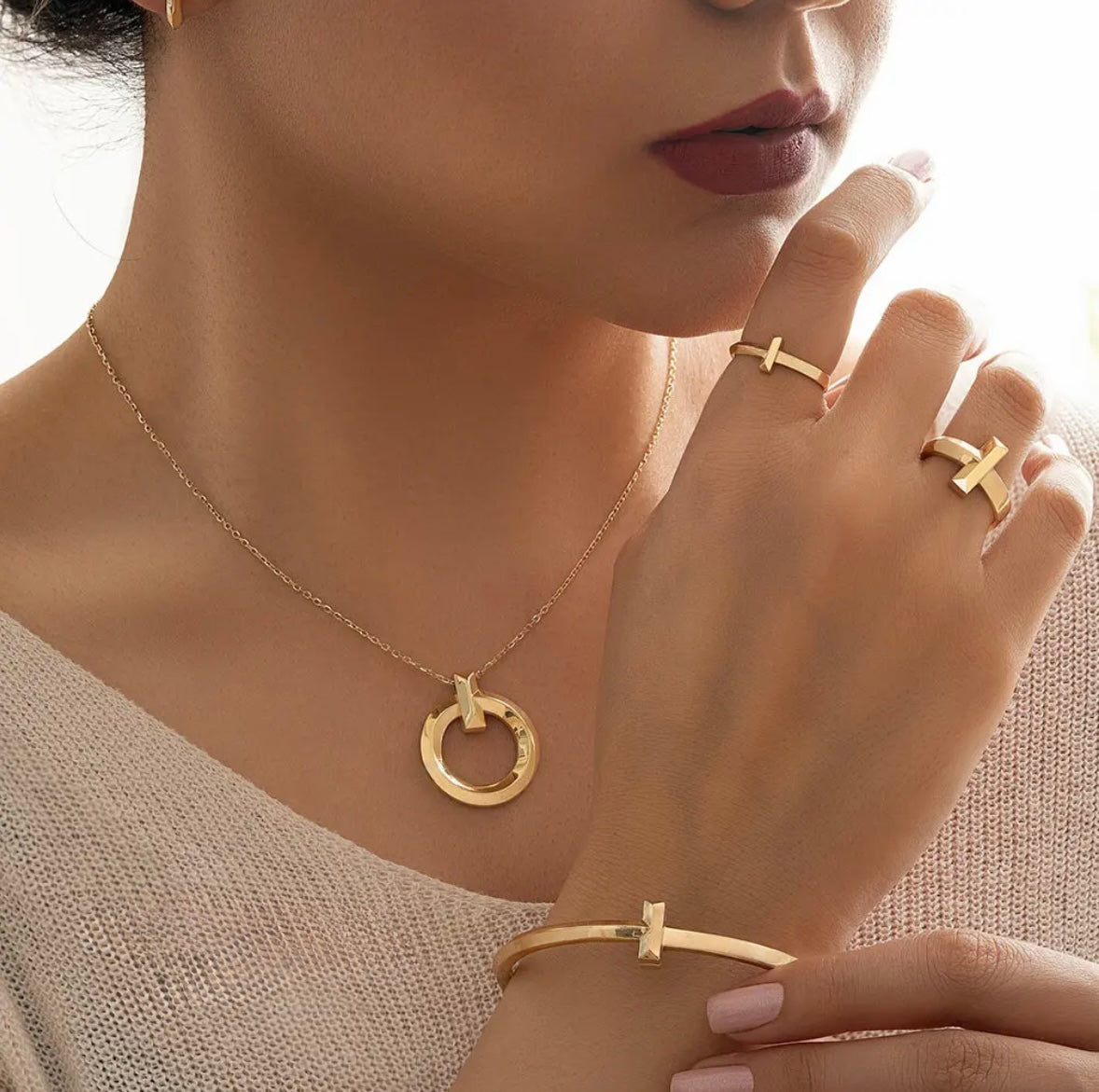 Gold necklace, rings, and bracelet on a model against a neutral background