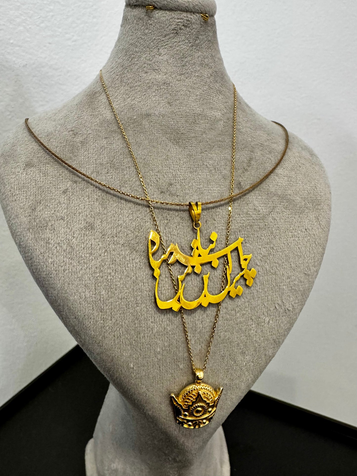 Gold necklace with an intricate pendant on a mannequin bust against a plain background