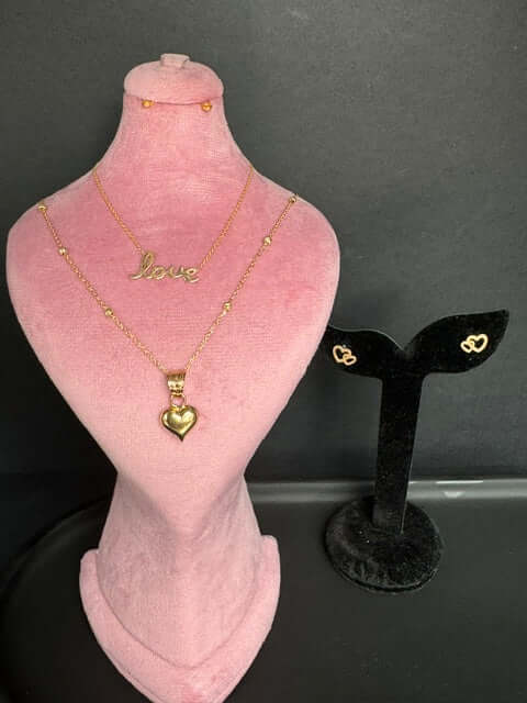 Puffy Heart Gold Pendant showcased on a pink display with love necklace and matching earrings in a jewelry collection.