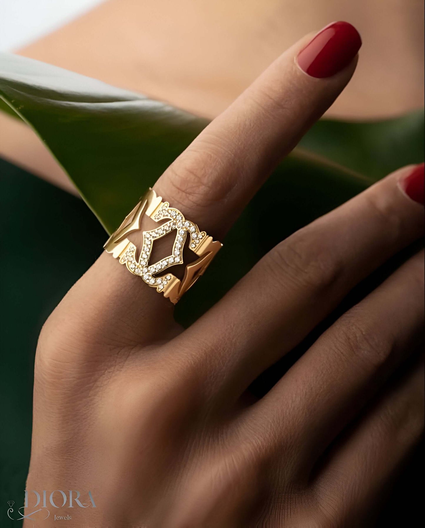 Elegant 18k Queen Gold Ring showcased on a hand with red nails, surrounded by green leaves, highlighting luxury and sophistication.