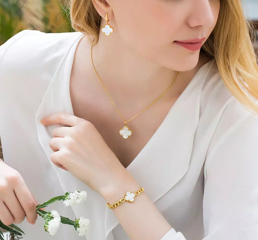 A person wearing a white outfit showcasing a gold necklace and bracelet with mother of pearl pendants.
