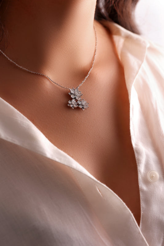 A person wearing a white shirt showcasing a silver necklace with a lotus flower shape pendant adorned with diamonds.