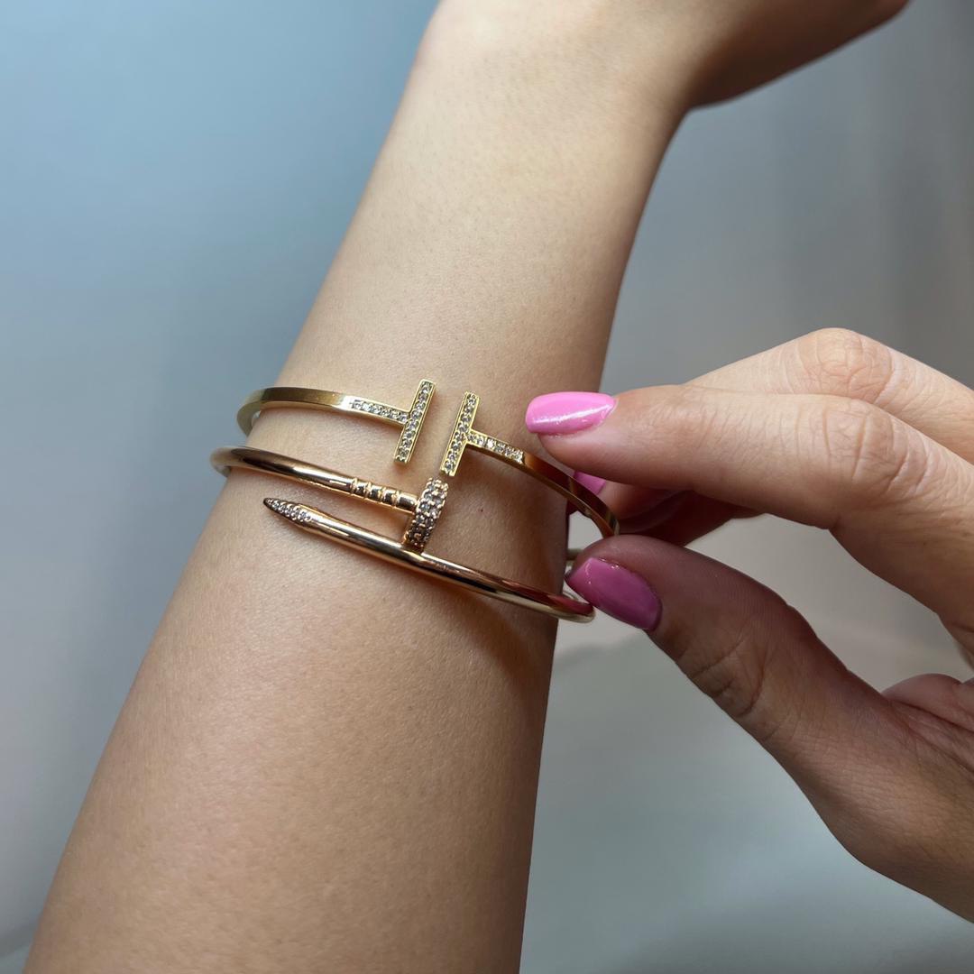 A person's arm wearing a gold nail bracelet with small gemstones.