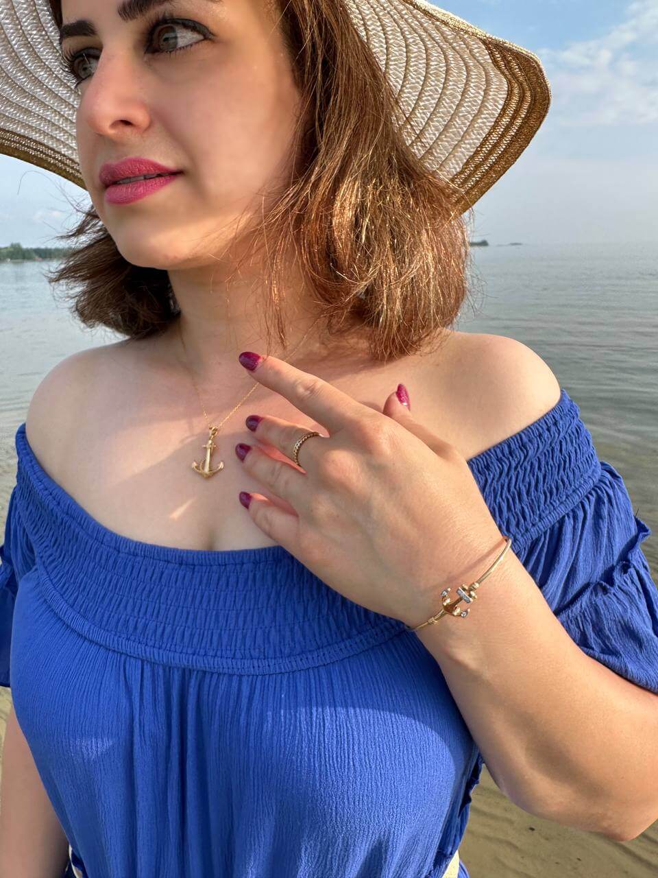 Woman wearing a Small Anchor Gold Pendant with an off-shoulder blue dress by the water.