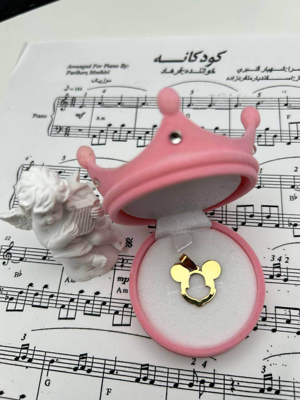 Mickey Mouse Pendant displayed in a pink crown-shaped jewelry box on sheet music.