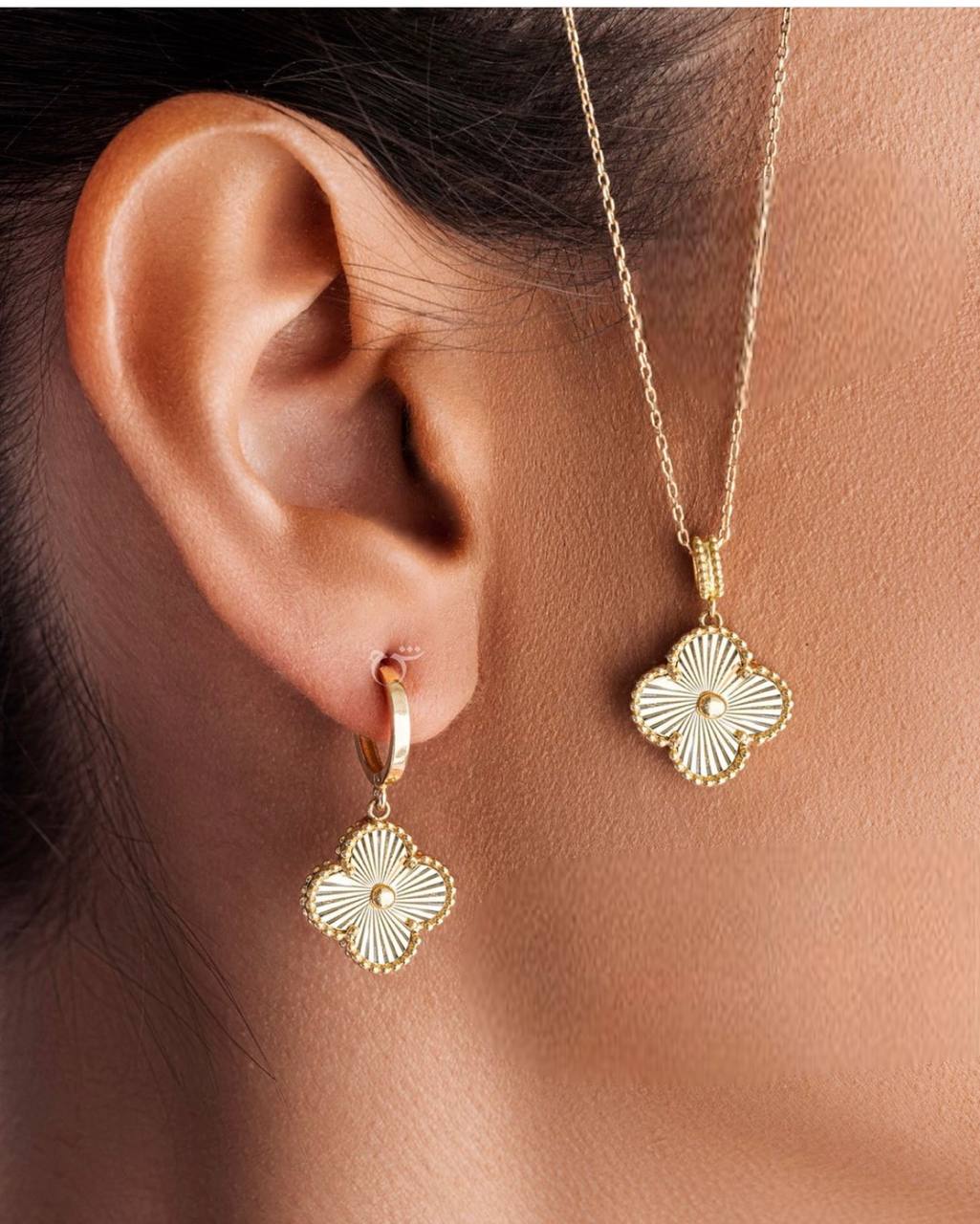 A person wearing a Van Cleef & Arpels gold pendant on a necklace and matching gold earrings.