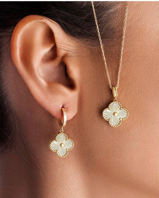 A person wearing a Van Cleef & Arpels gold pendant on a necklace and matching gold earrings.