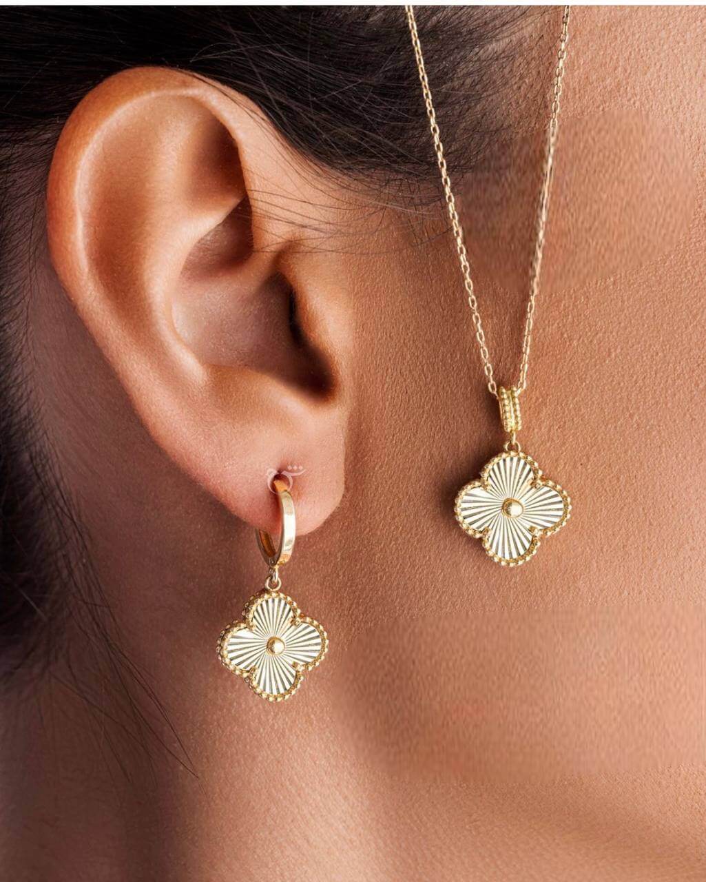 A person wearing a Van Cleef & Arpels gold pendant on a necklace and matching gold earrings.