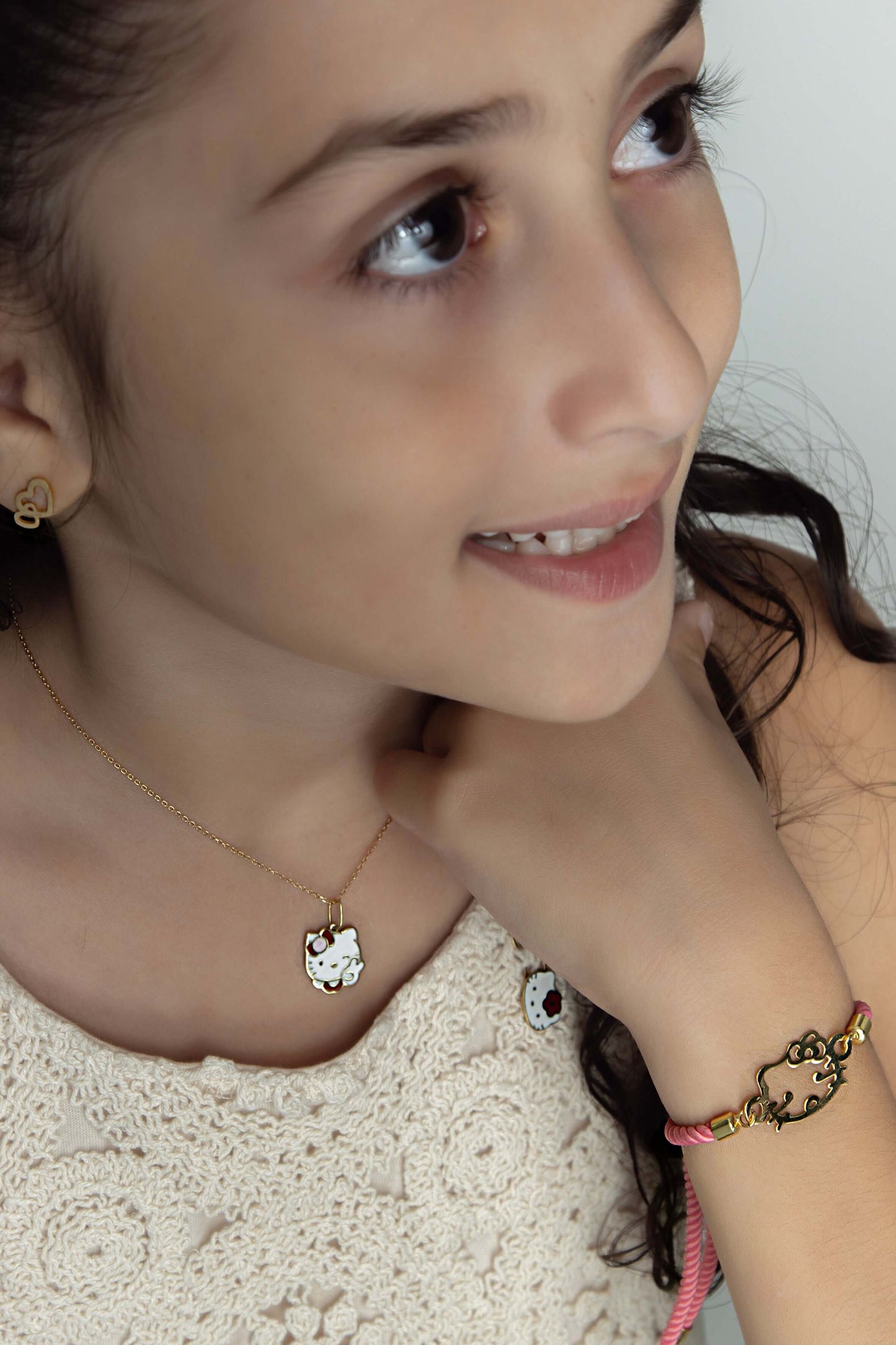 A young girl wearing a White Kitty Pendant necklace and matching bracelet, showcasing delightful jewelry accessories.
