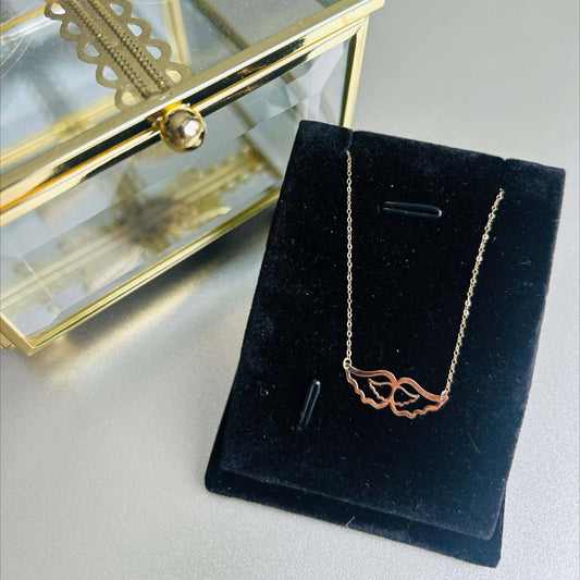 18K Gold Angel Wings Necklace displayed on a black velvet stand next to a glass jewelry box.