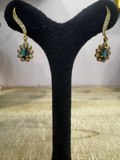 Gold earrings with green gemstones on a black stand against a neutral background