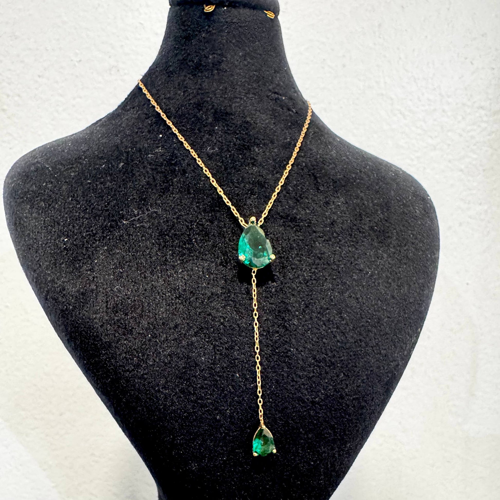 Gold necklace with green gemstones on a black mannequin bust.