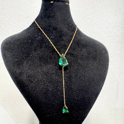 Gold necklace with green gemstones on a black mannequin bust.