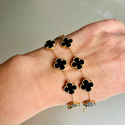 Bracelet with black clover-shaped charms on a wrist against a neutral background